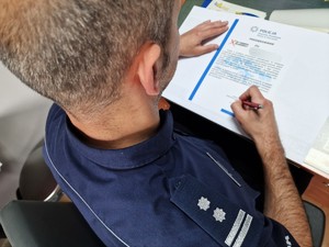 Zdjęcie przedstawia policjanta podpisującego dokument.