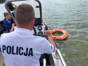 Zdjęcie przedstawia: koło ratunkowe w wodzie. Widoczny także policjant na łodzi.