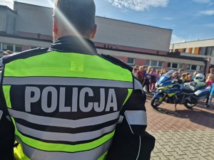Zdjęcie przedstawia: policjanta przed grupą dzieci, z tyłu widoczny policyjny motocykl.