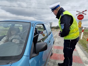 Zdjęcie przedstawia: policjanta podczas rozmowy z kierowcą samochodu przy przejeździe kolejowym.