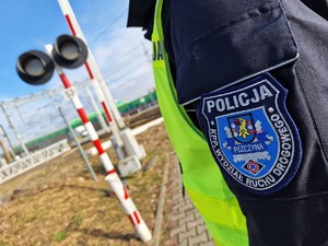Zdjęcie przedstawia: naszywkę Komendy Powiatowej Policji w Pszczynie, z tyłu widoczny sygnalizator kolejowy.